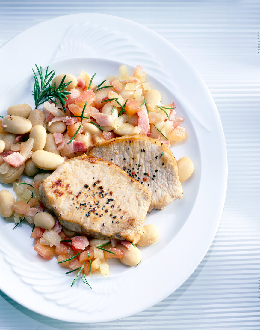 Pork chops with white beans, onions, bacon and rosemary on plate