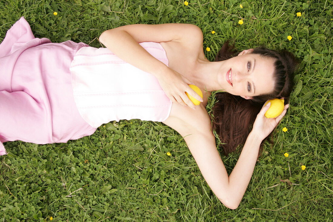 Frau liegt im Gras, hält sich Zitrone an Schulter und Kopf