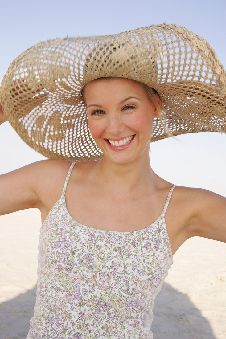 Jennifer Frau hält d. Sonnenhut am Kopf fest, fröhlich, am Strand