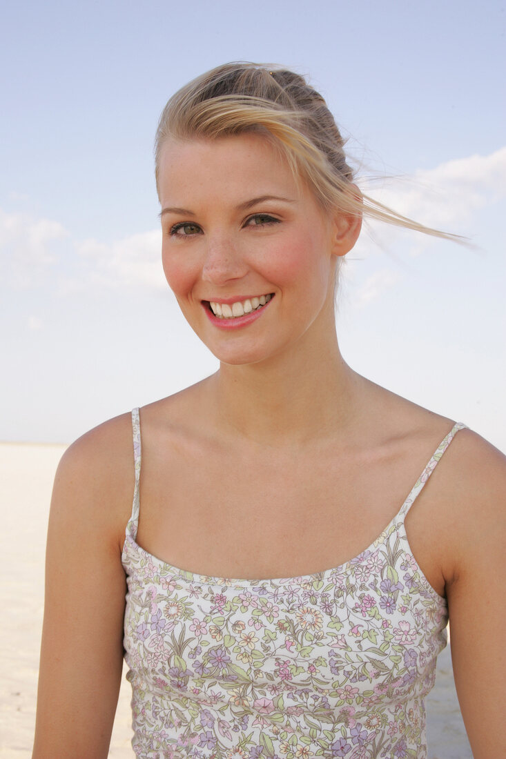 JenniferBlonde Frau mit Zopf und in geblühmten Top am Strand lacht