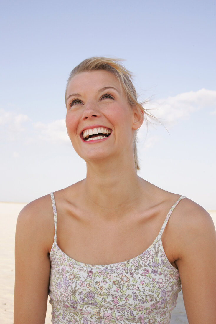 Portrait of beautiful woman in floral pattern dress standing on beach, smiling