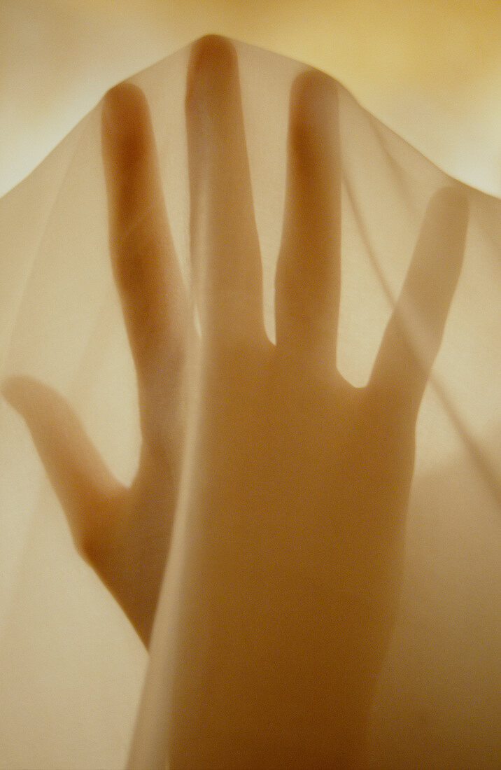Frauenhand mit gespreizten Fingern unter einem transparenten Tuch