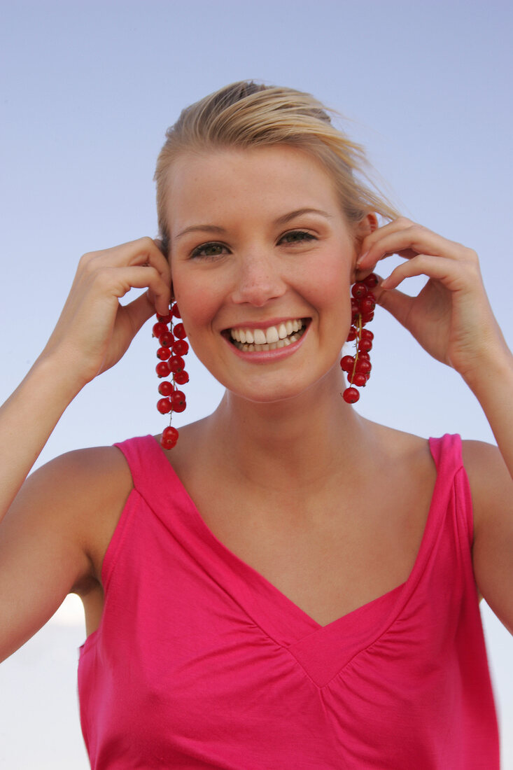 Blonde woman holding currant branches to her ears, smiling
