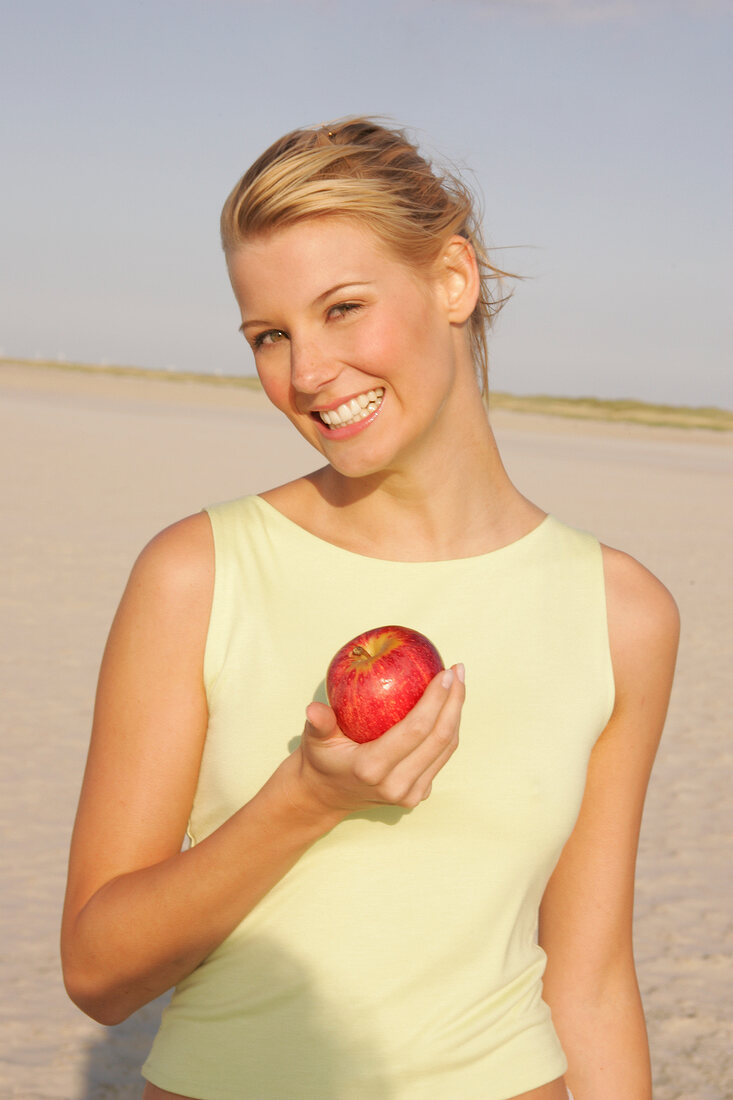 Jennifer Frau am Strand hält einen roten Apfel in der Hand, lacht