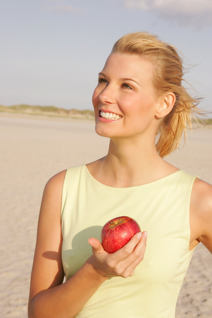 Jennifer Frau am Strand steht seitlich mit e. Apfel in der Hand