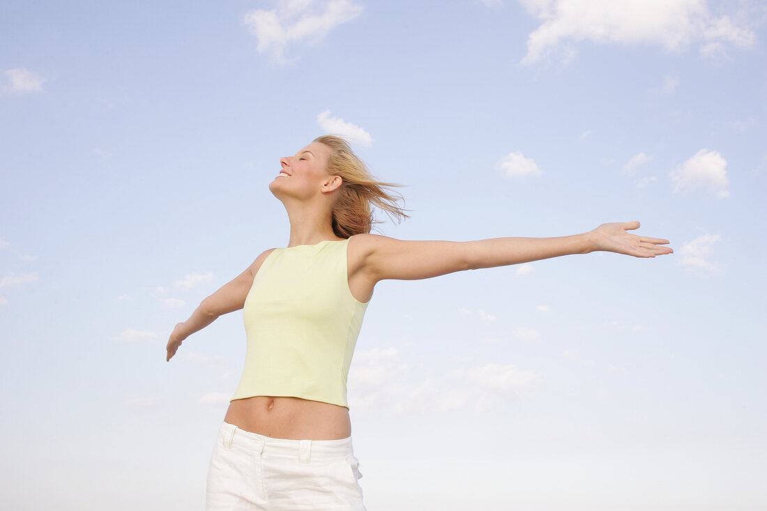 Happy woman with windswept hair smiling with arms outstretched, eyes closed