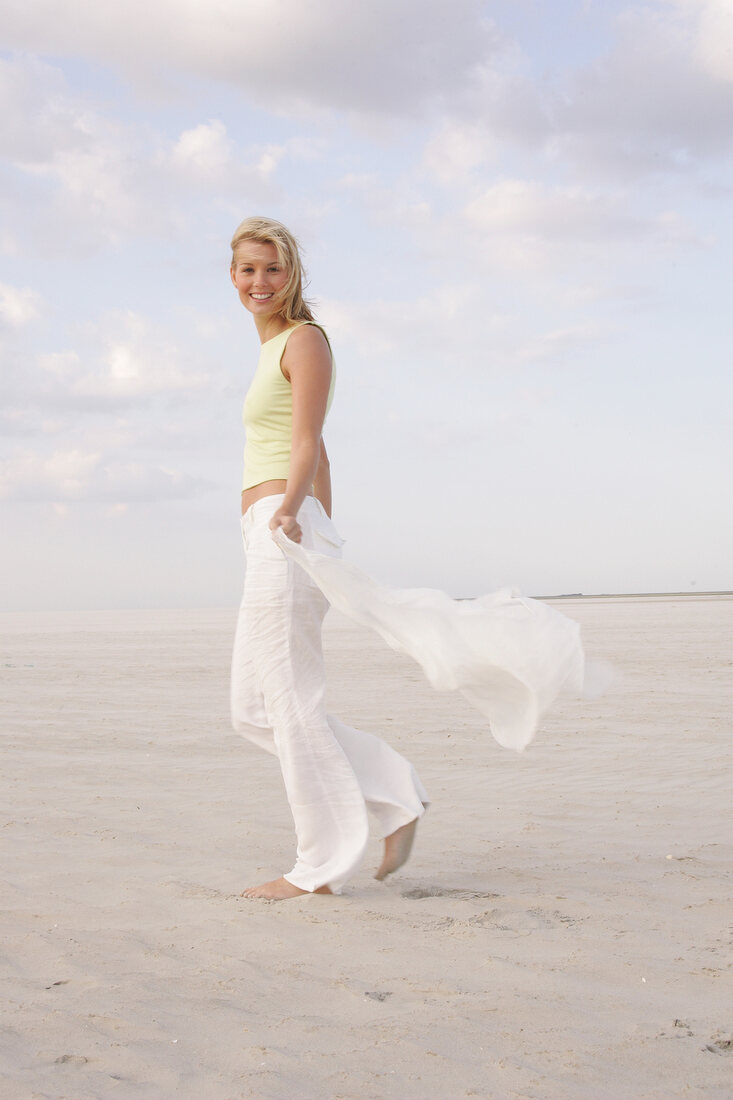 Portrait of beautiful woman holding scarf and walking on beach, smiling