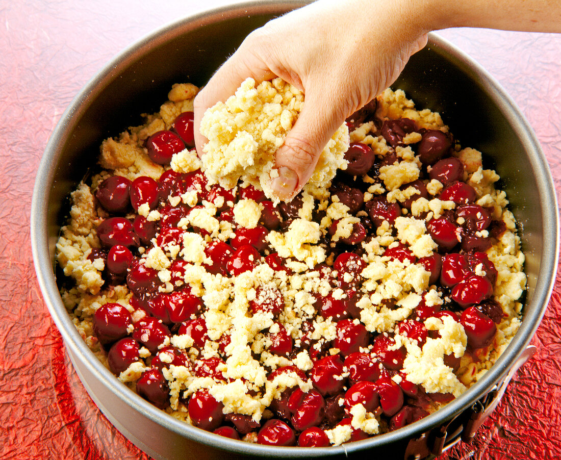 Streusel teig being sprinkled on cherries into pan