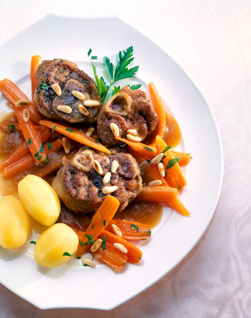 Lamb shank with carrots, potatoes, pine nuts and parsley on dish