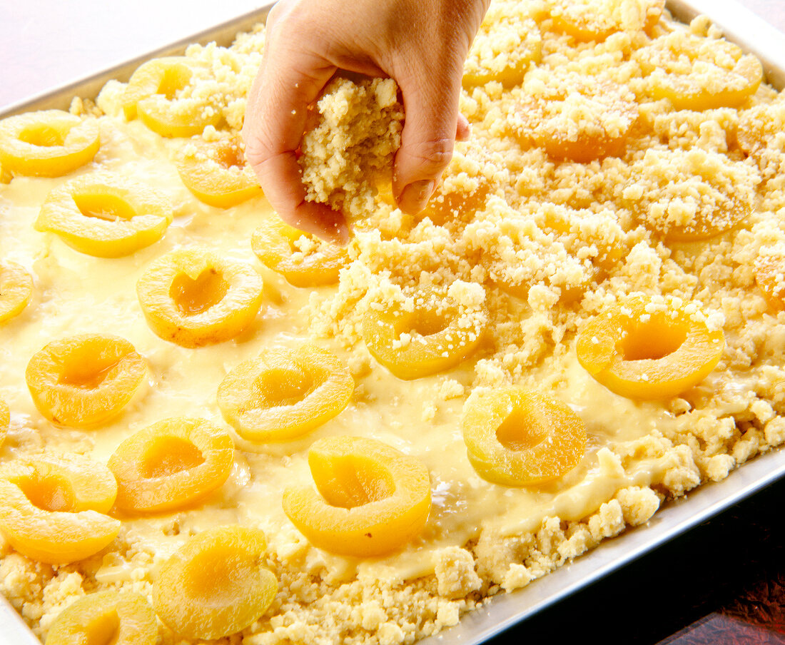 Streusel teig being sprinkled on apricots in baking tray