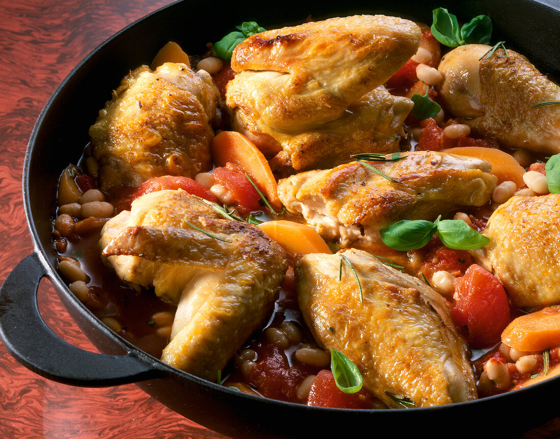 Close-up of baked chicken with tomato sauce, beans, carrots and basil in casserole