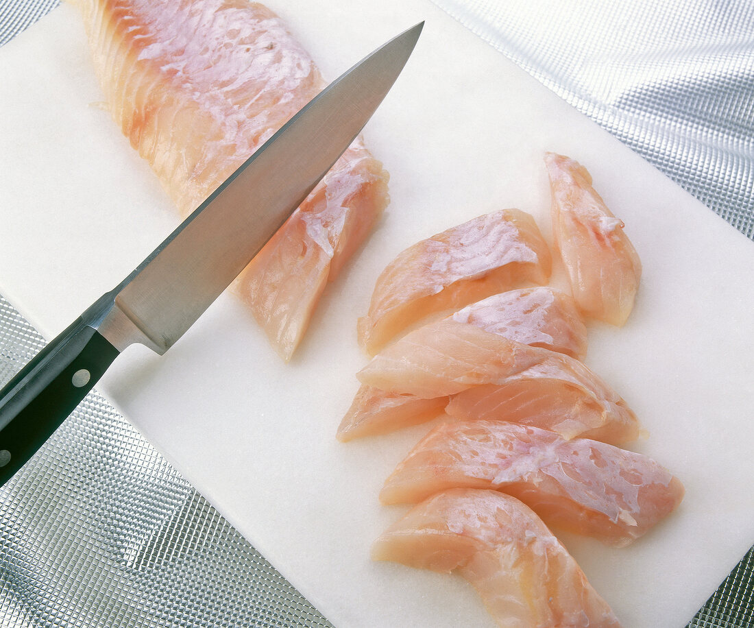 Redfish fillet being cut with knife on cutting board