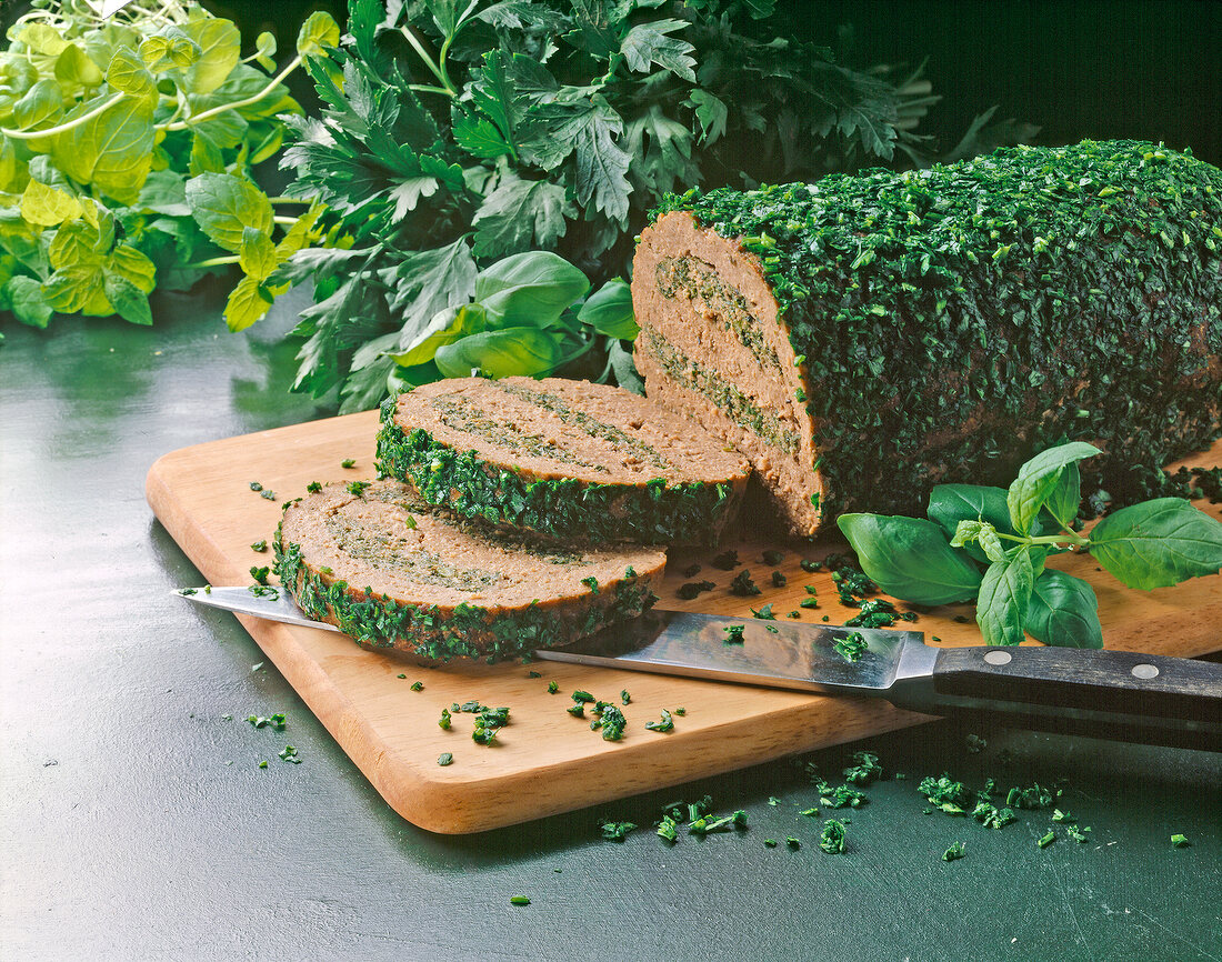 Meatloaf and slices of it coated with various fresh herbs on cutting board