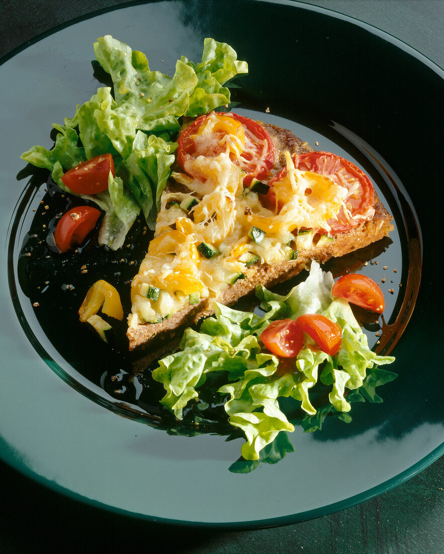 Piece of mince pie with fresh vegetable salad on black dish