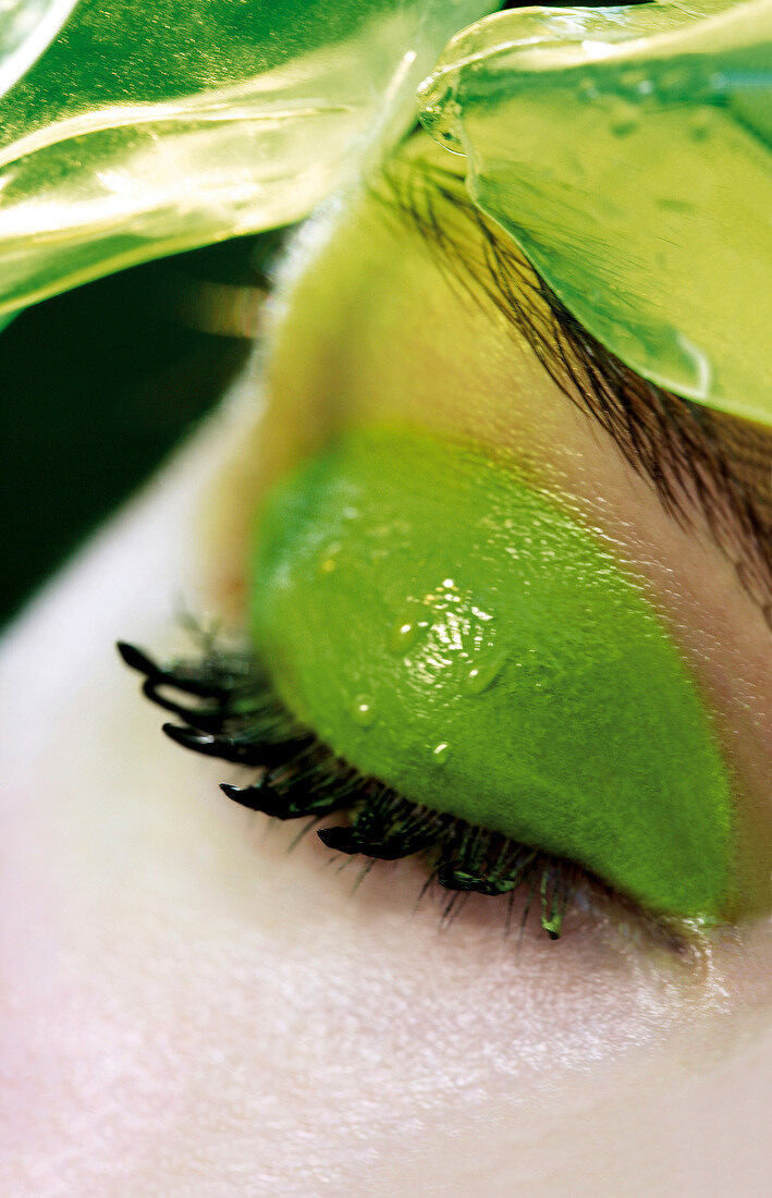 Extreme close-up of woman wearing green eye shadow and mascara with water droplets