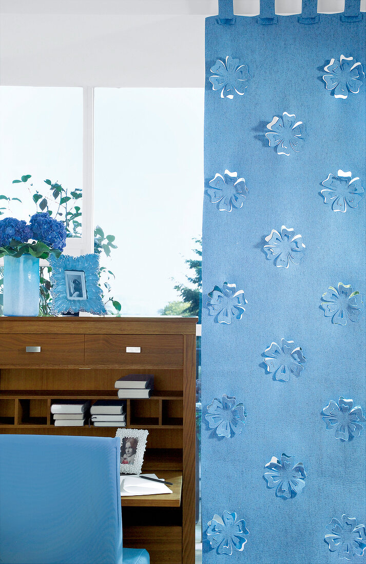 Blauer Filzvorhang mit ausgestanzten Blüten neben modernem Sekretär
