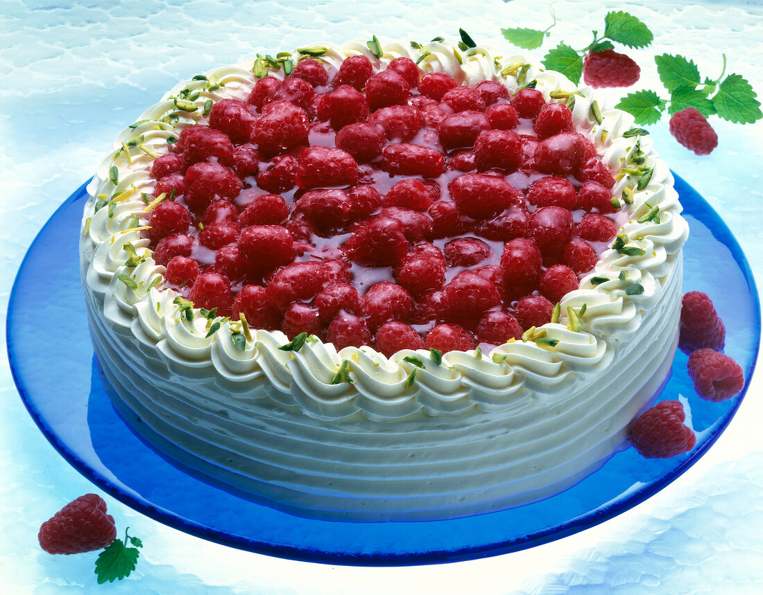 Raspberry cake on blue plate with raspberries being scattered