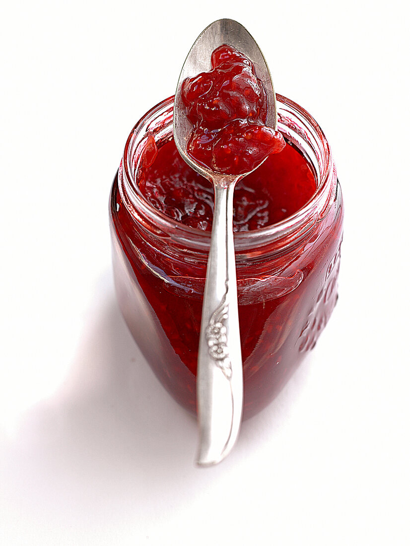 Glass jar of prosecco raspberry jam with spoon on it
