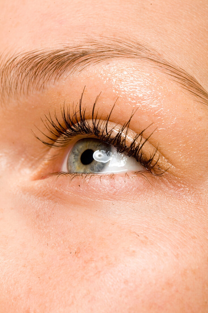 Extreme close-up of woman's gray eye with long eyelashes wearing golden eye shadow