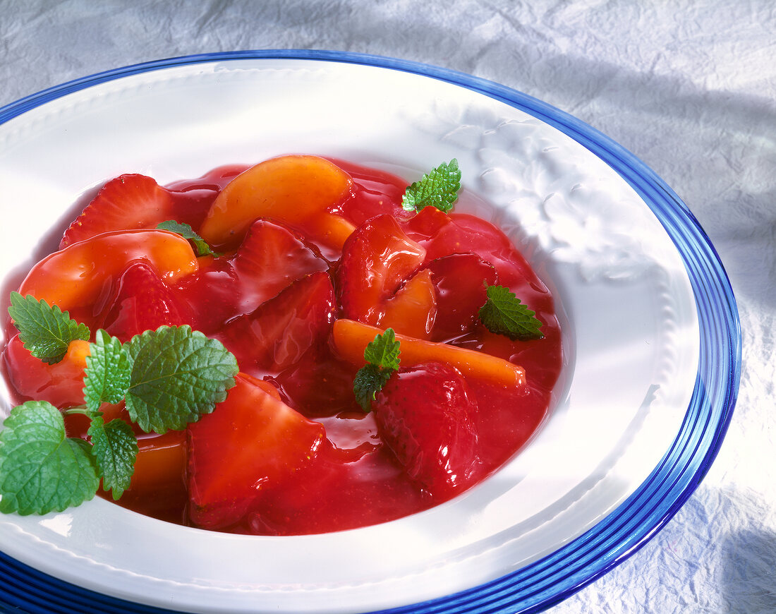 Rote Grütze mit Erdbeeren und Pfirsichen, garniert mit Melisse.
