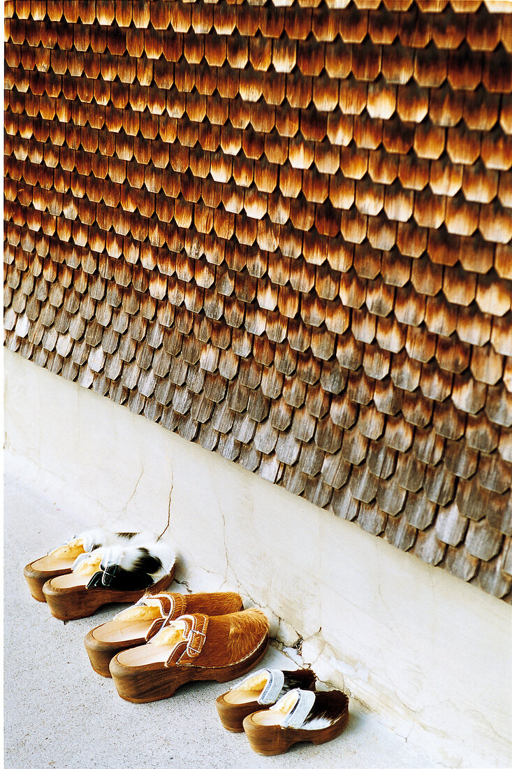 Holzschuhe mit Rindsfell stehen vor einer Hauswand mit Schindeln, 3 Paar