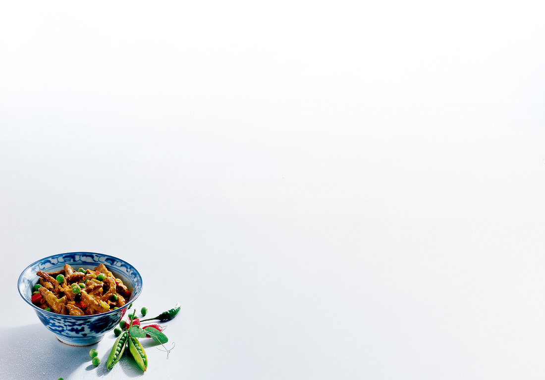 Beef curry with peppers and peas in bowl on white background