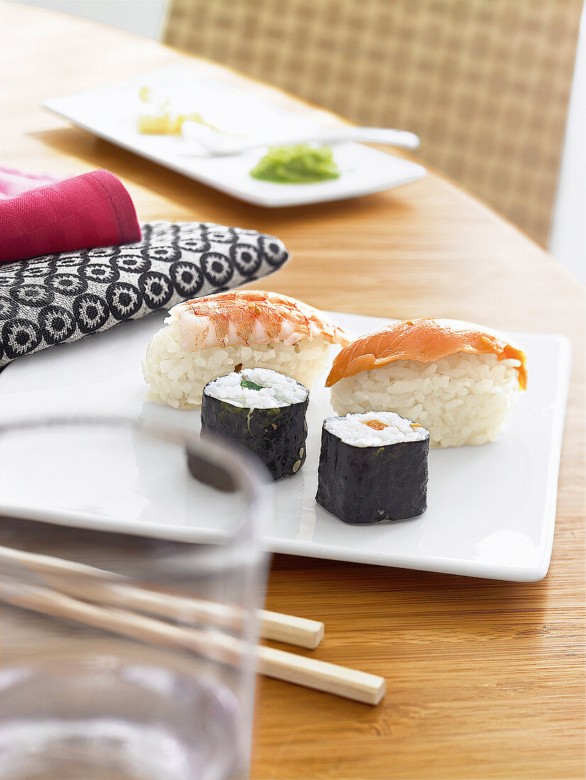 Sushi stilgerecht auf flachem Teller und mit Stäbchen.