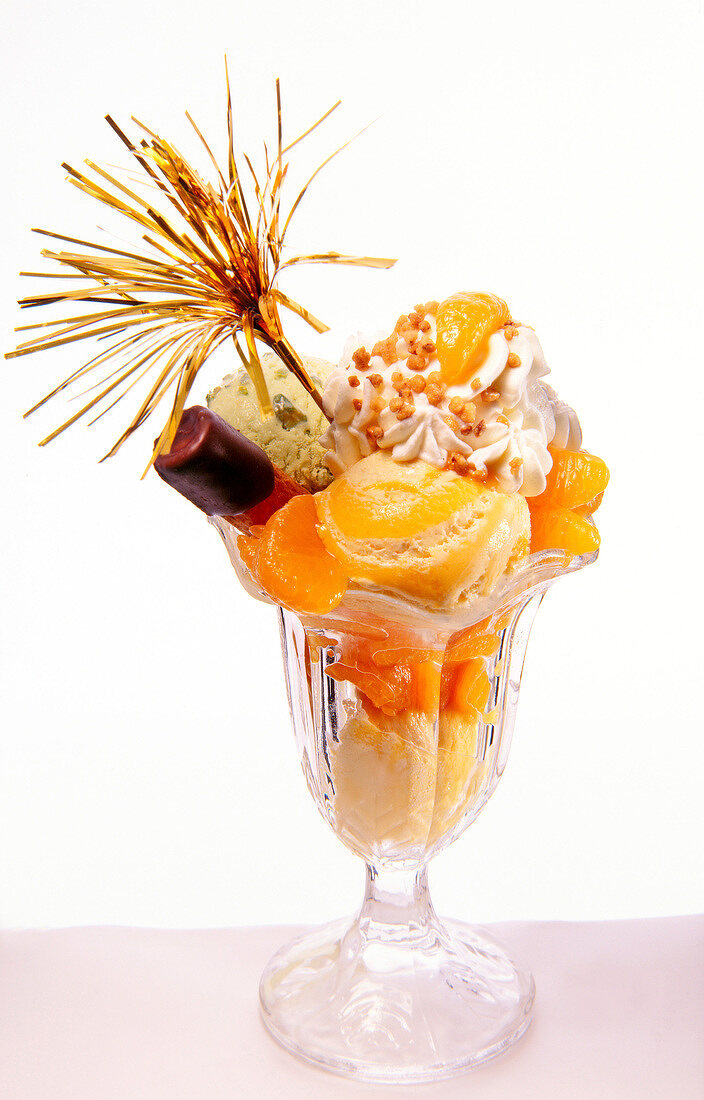 Four scoops of ice cream with mandarin oranges, cream and nut brittle in glass