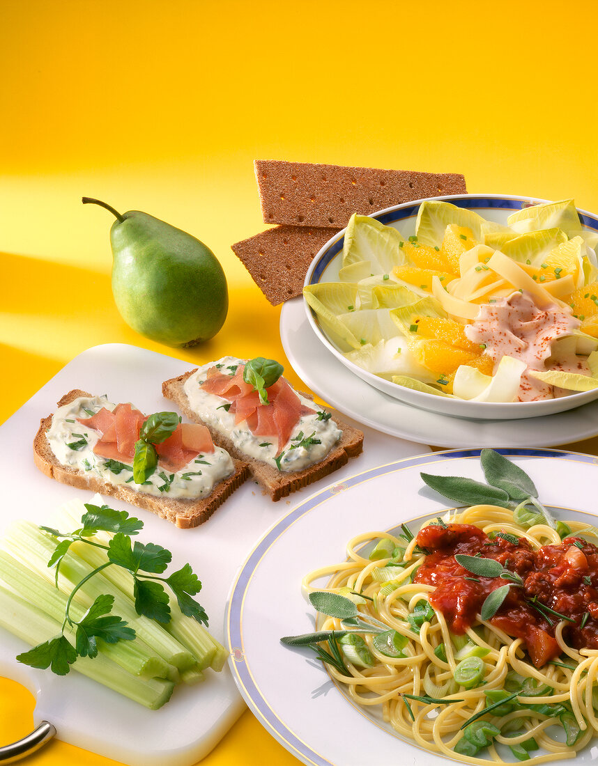Close-up of spaghetti, chicory cheese salad, bread with cream cheese, pears and celery
