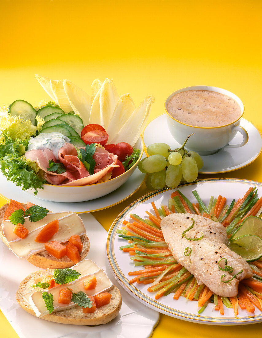 Close-up of salad, cappuccino, fish fillet with vegetables and bread with camembert