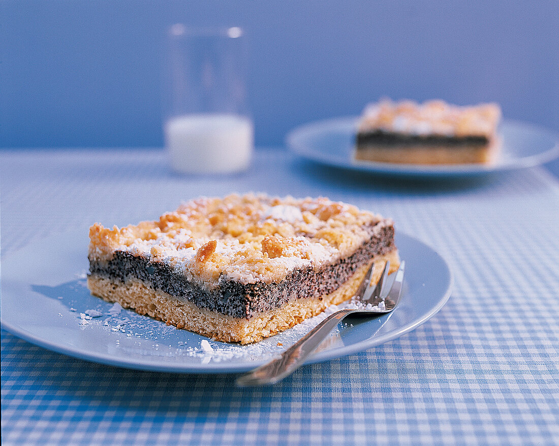 Mohn-Streuselkuchen auf einem blauen Teller mit Kuchengabel, Puderzucker