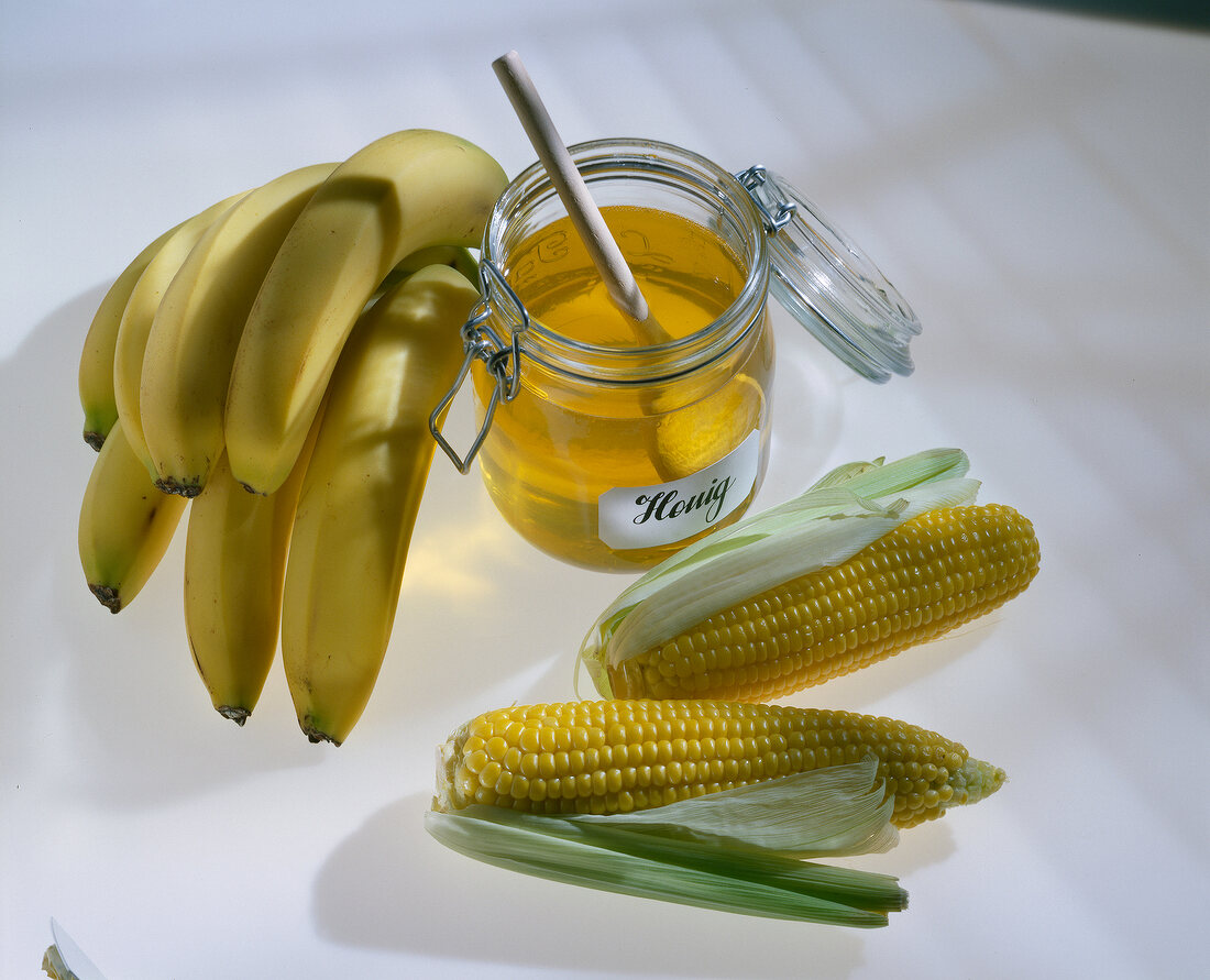 Close-up of bananas, corn and bottle of honey on white background