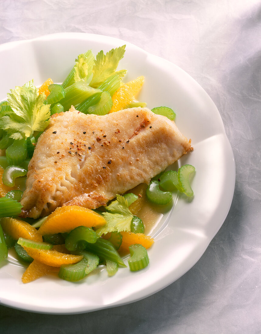 Close-up of redfish fillet with celery and orange slices in bowl