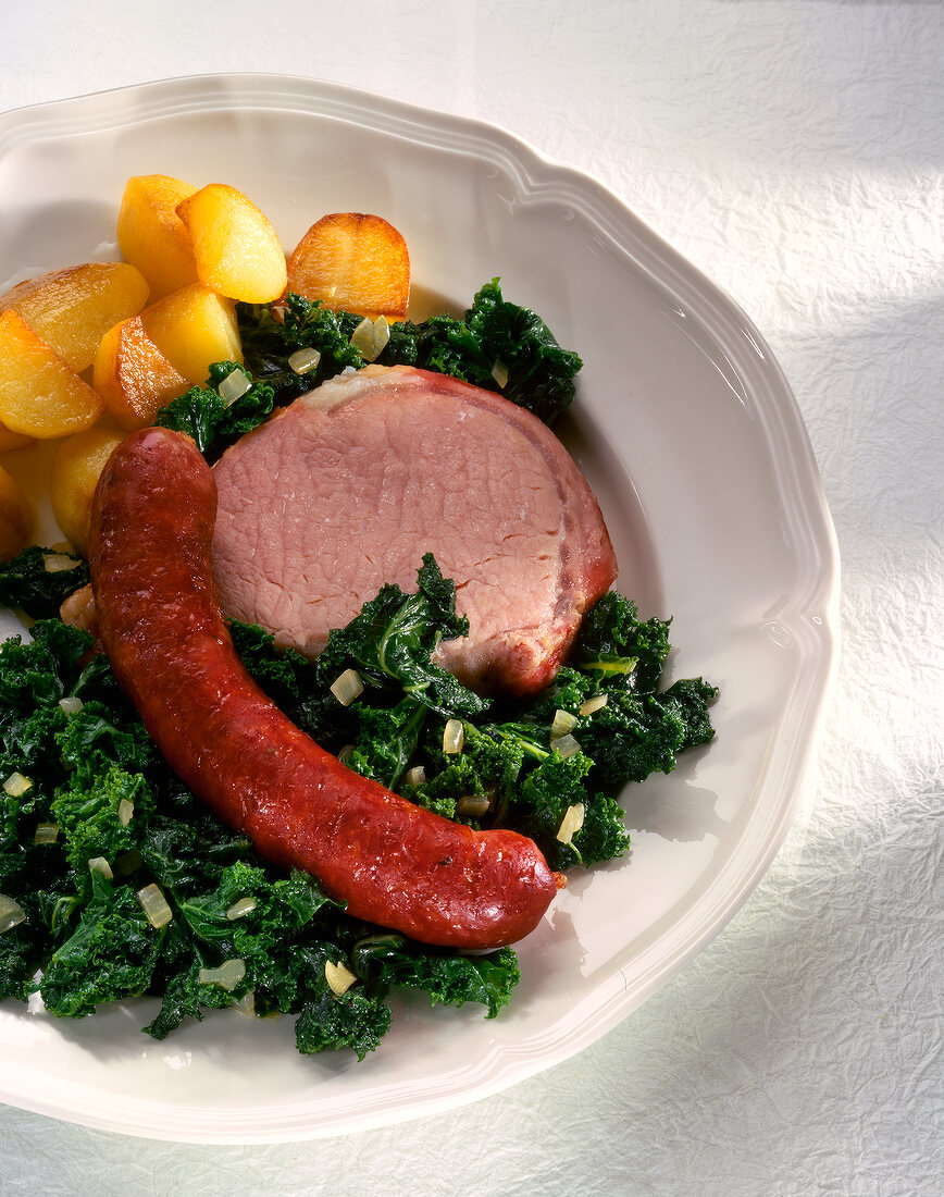 Close-up of kale with smoked pork, sausage meat and roast potatoes in dish