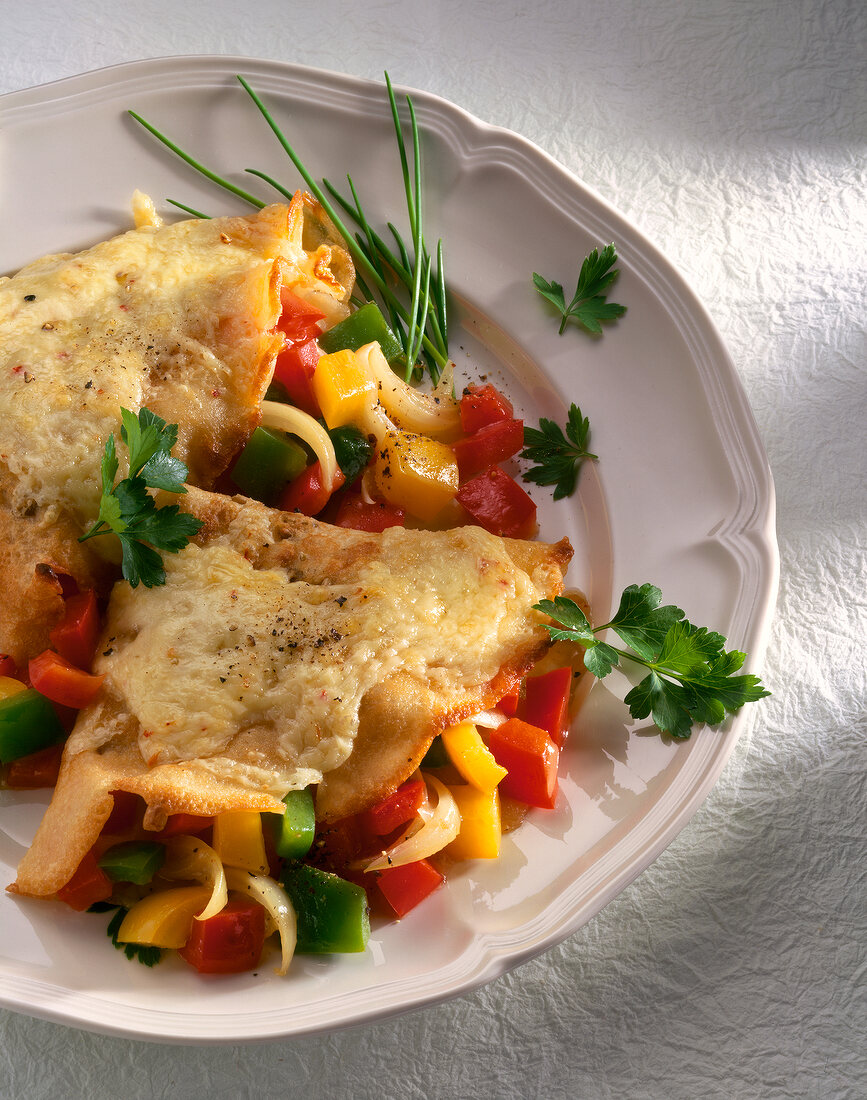 Close-up of pancakes stuffed with cheese and topped with peppers and onions in dish