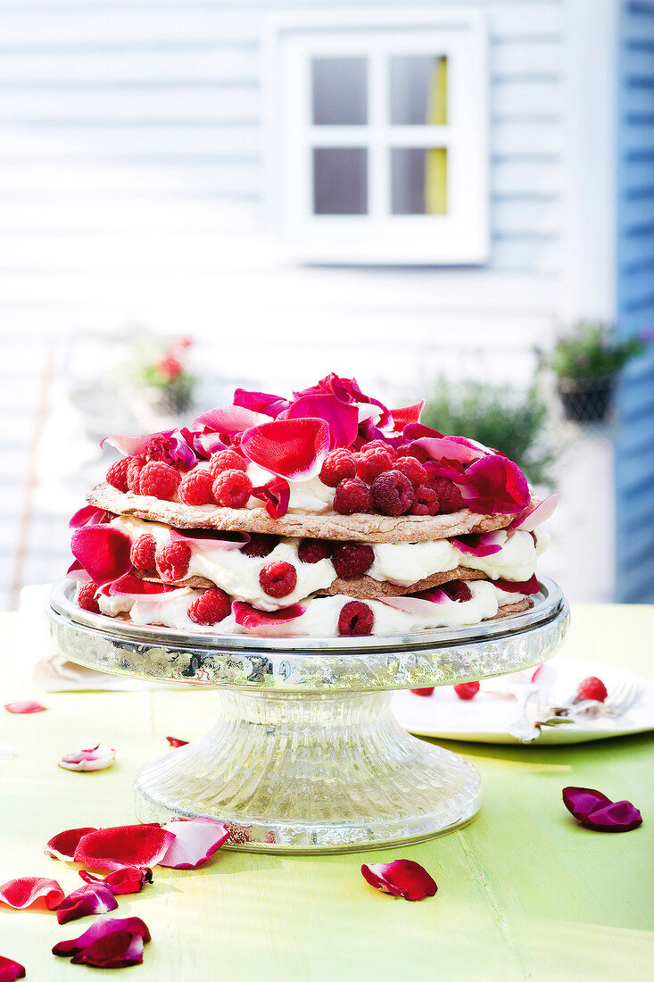 Almond and raspberries cream cake decorated with rose petals on cakestand