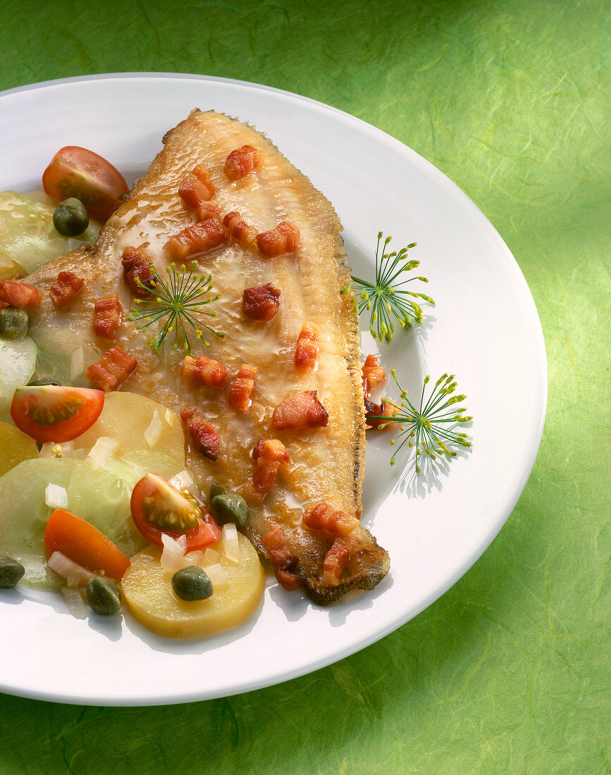 Plaice fillet with bacon, potatoes and salad on plate