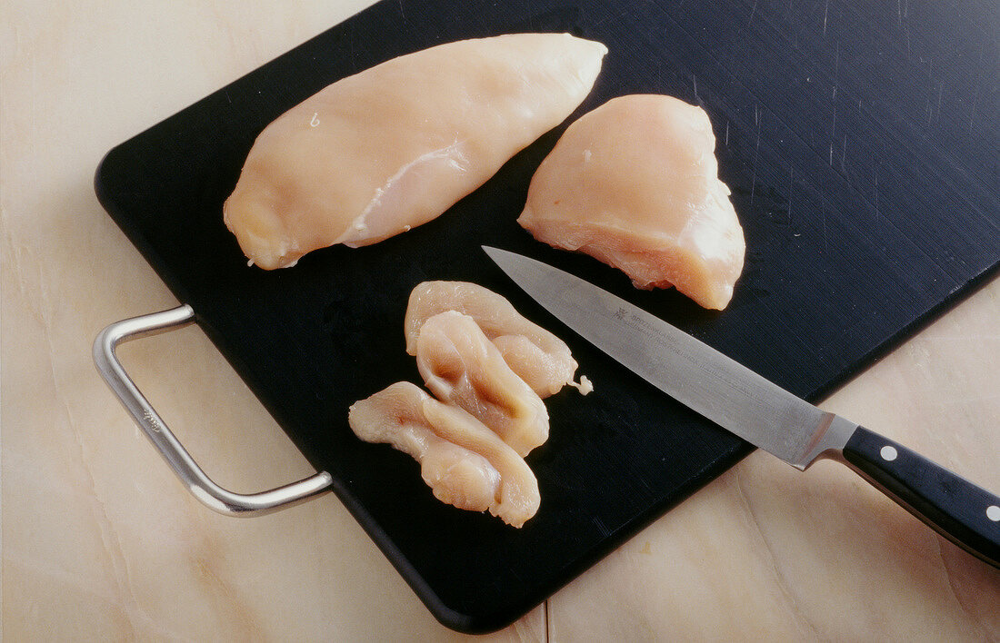 Chicken breasts being cut into strips with knife