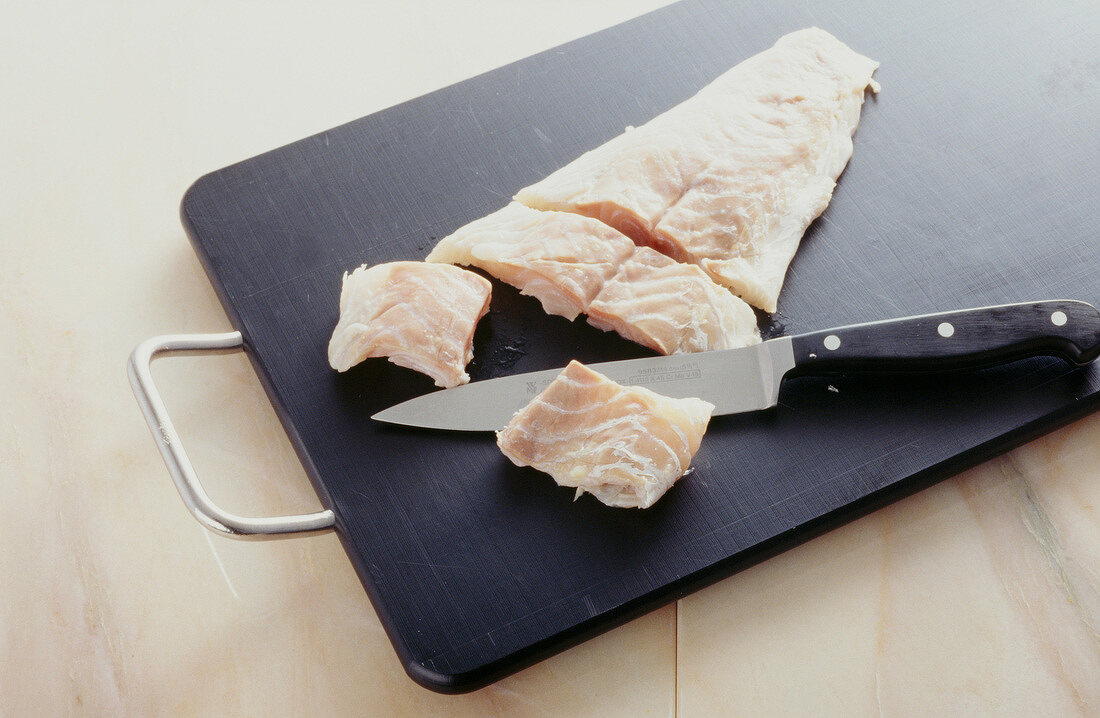 Salmon fillet being cut into pieces with knife on chopping board