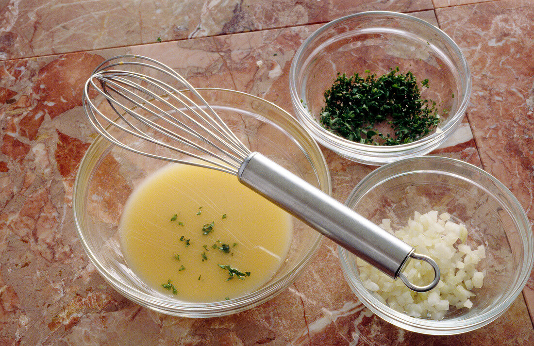 Chopped herbs and onions added to vinegar and mustard mixture in bowl with whisk, step 2