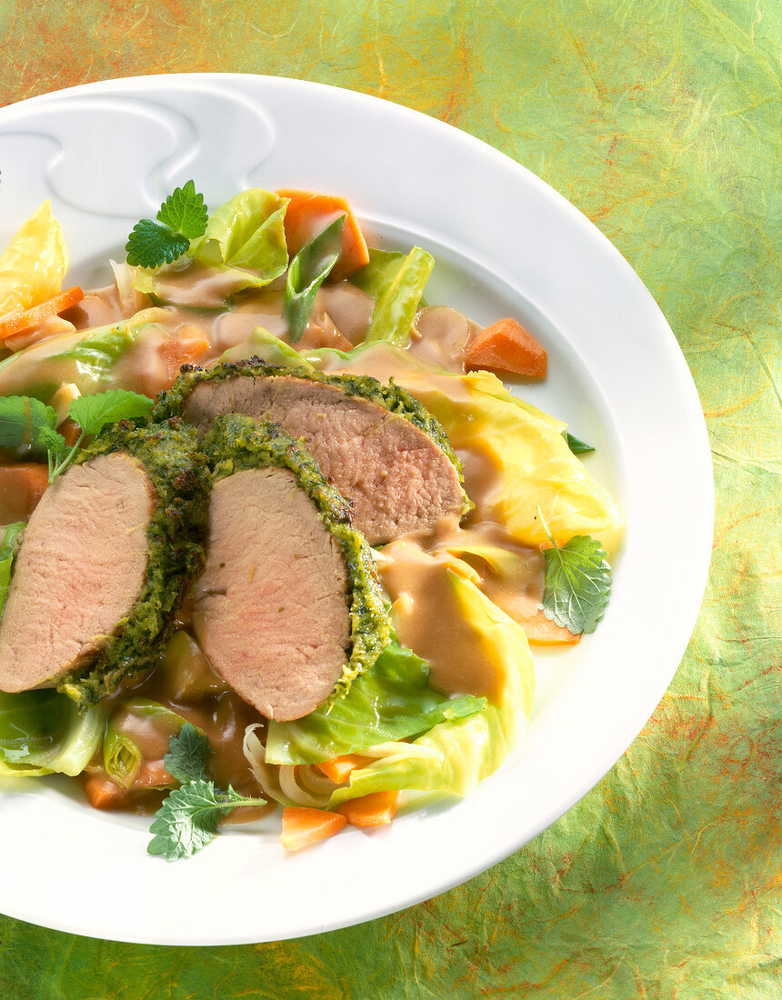 Close-up of pork fillet with vegetables and herb crust on plate