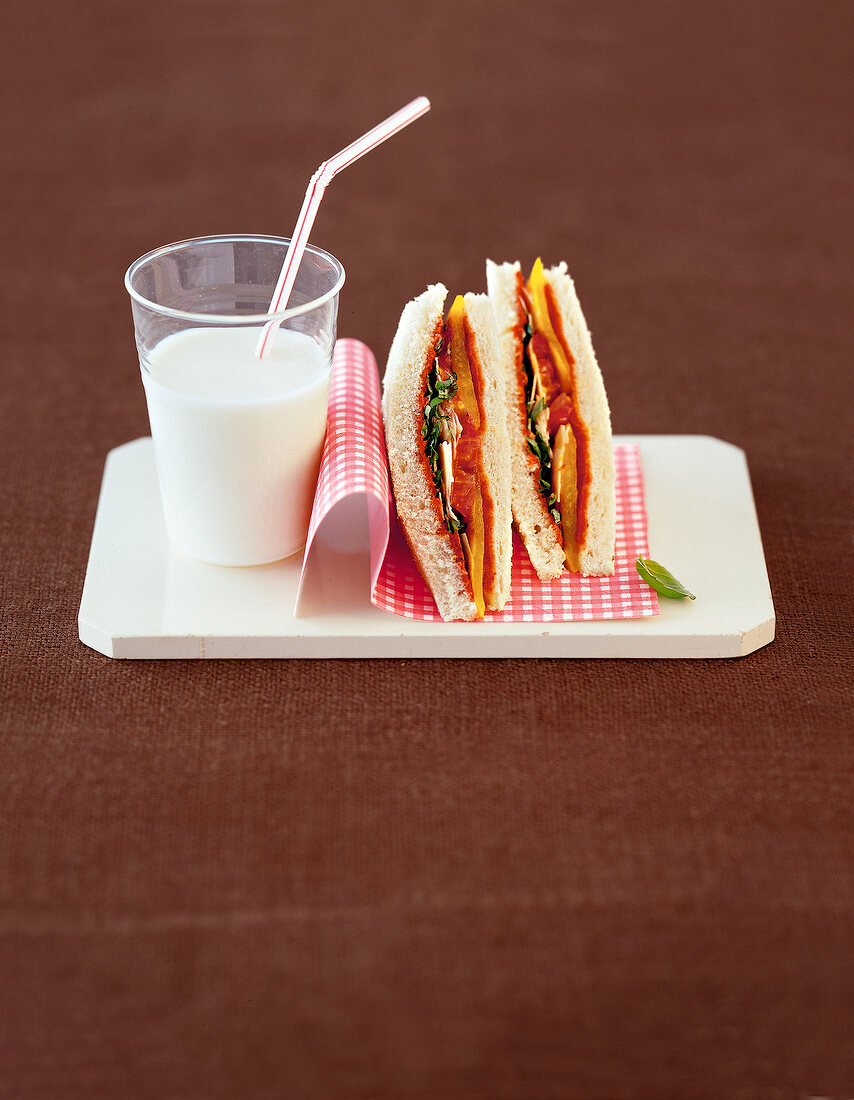 Vegetable sandwich and glass of milk with straw on serving dish