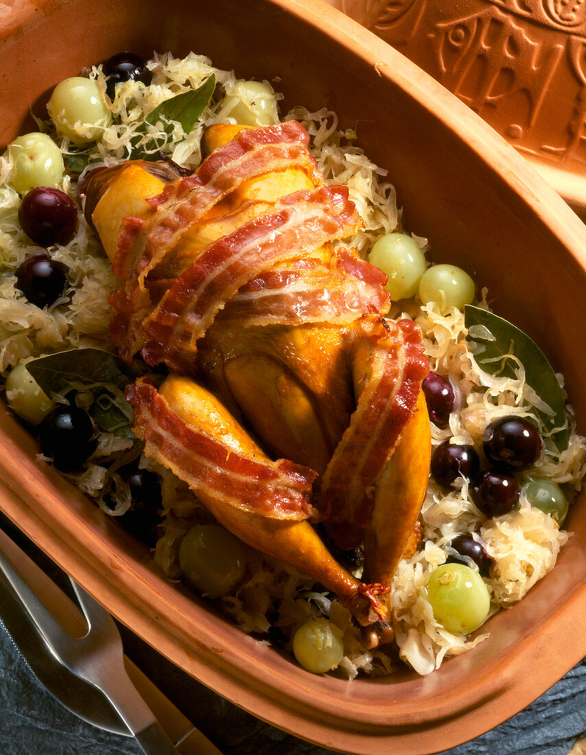 Close-up of roasted pheasant on sauerkraut with grapes in serving dish