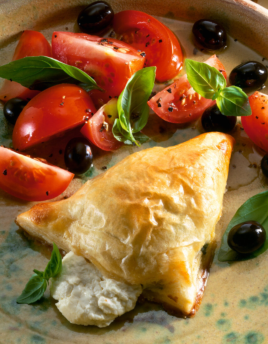 Close-up of puff pastry cheese pockets with basil, tomatoes and olives