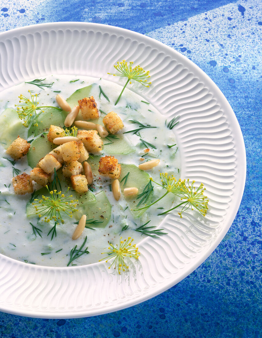 Close-up of cold cucumber soup with pine nuts, dill, parsley and croutons on plate