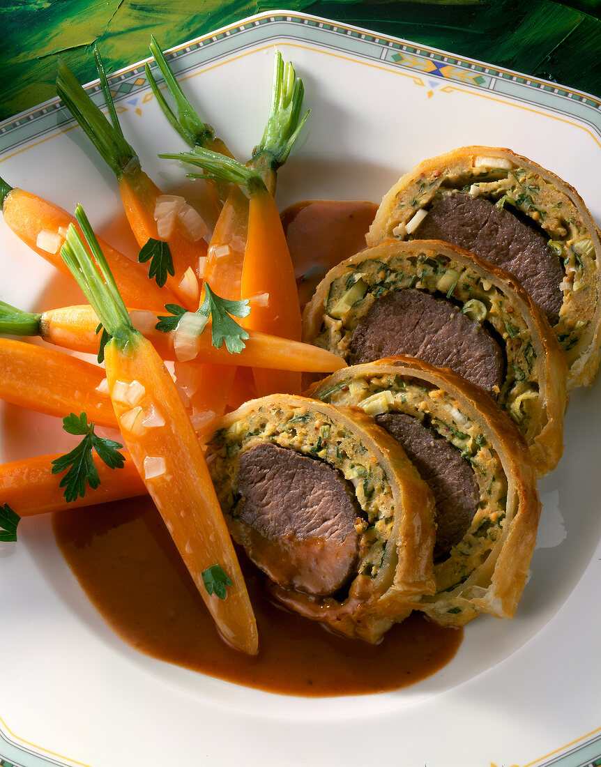 Close-up of venison fillet in puff pastry with carrots on plate