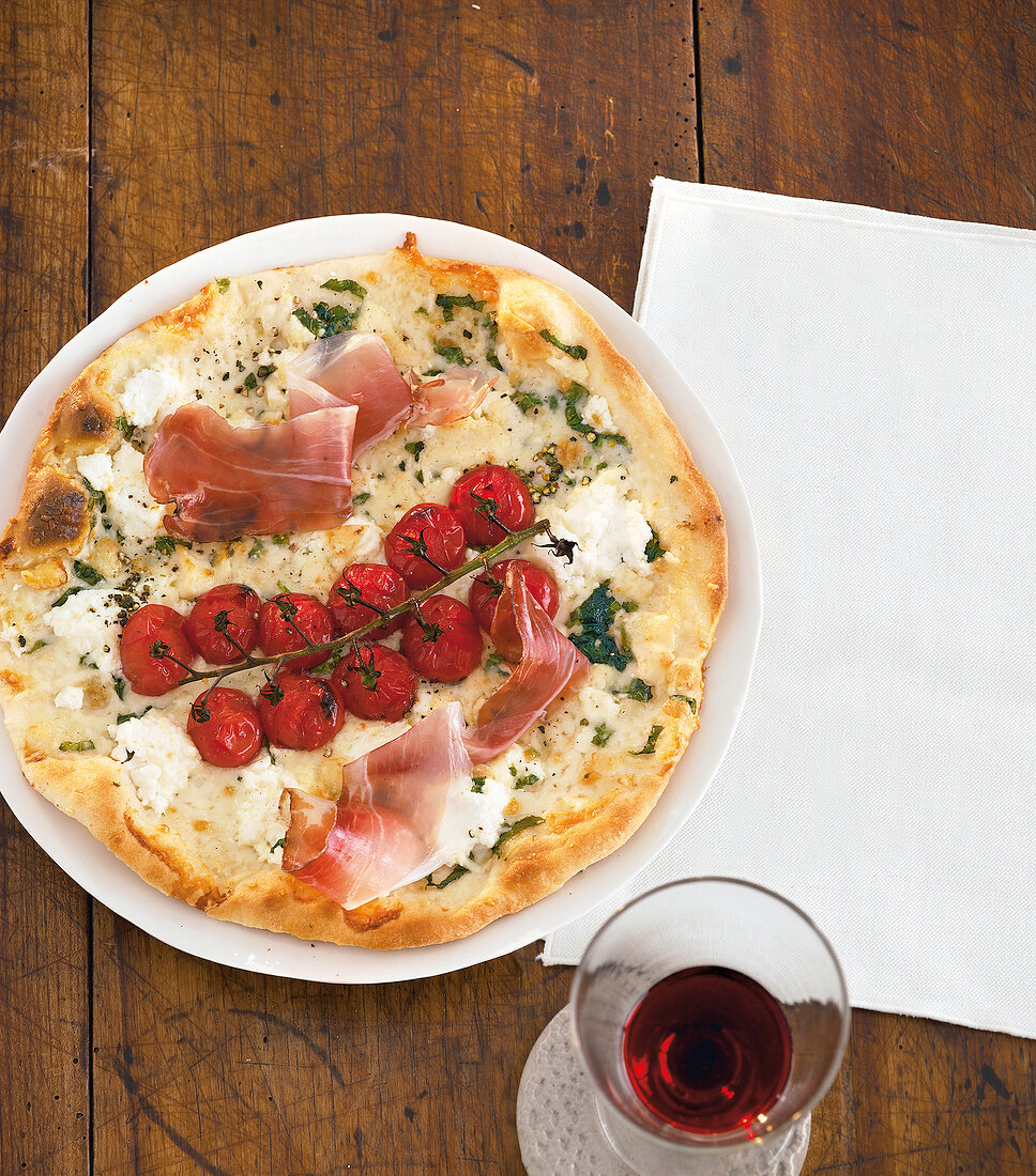 Round pizza with cheese, tomatoes, razor thin slices of ham on plate