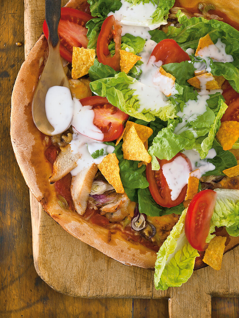 Close-up of tostada pizza with chicken, beans, cream cheese, tomato, lettuce, tortilla