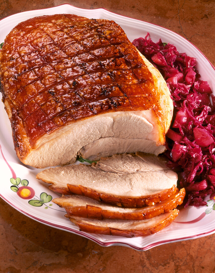 Sliced roast pork with apple, red cabbage and golden brown on plate