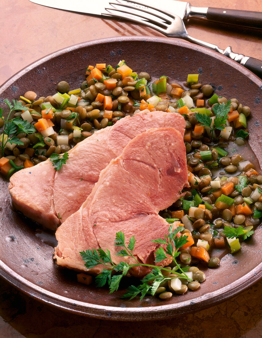 Close-up of shoulder of pork with herb lentils on plate